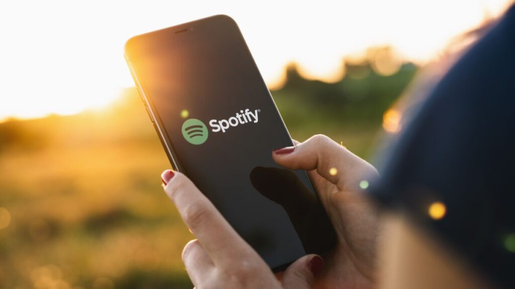 Woman holding phone in field with Spotify app onscreen
