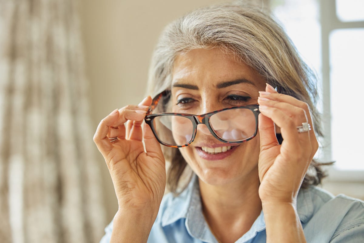 Mulher experimentando óculos em casa.